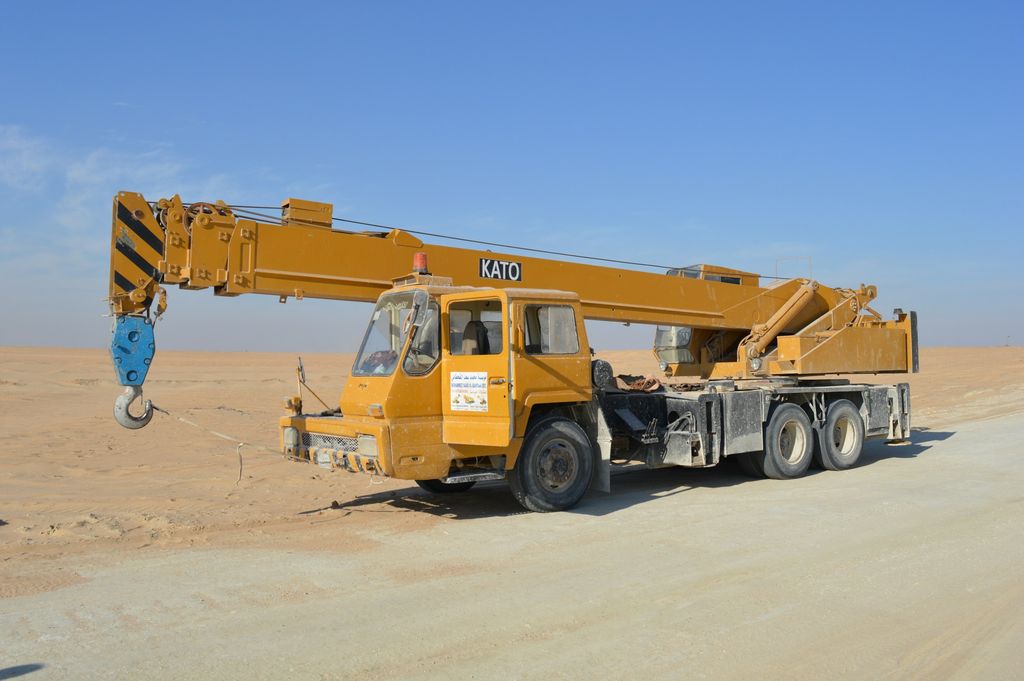 Yellow hydraulic truck crane parked on open desert ground under a clear sky